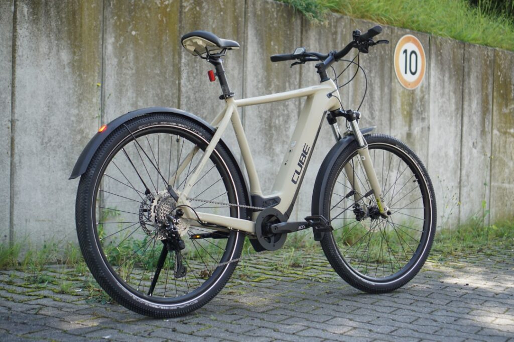 Cube Nuride Hybrid Pro 625 2022 Allroad, E-Bike mit robustem Rahmen, Scheibenbremsen und Schutzblechen auf gepflastertem Weg.
