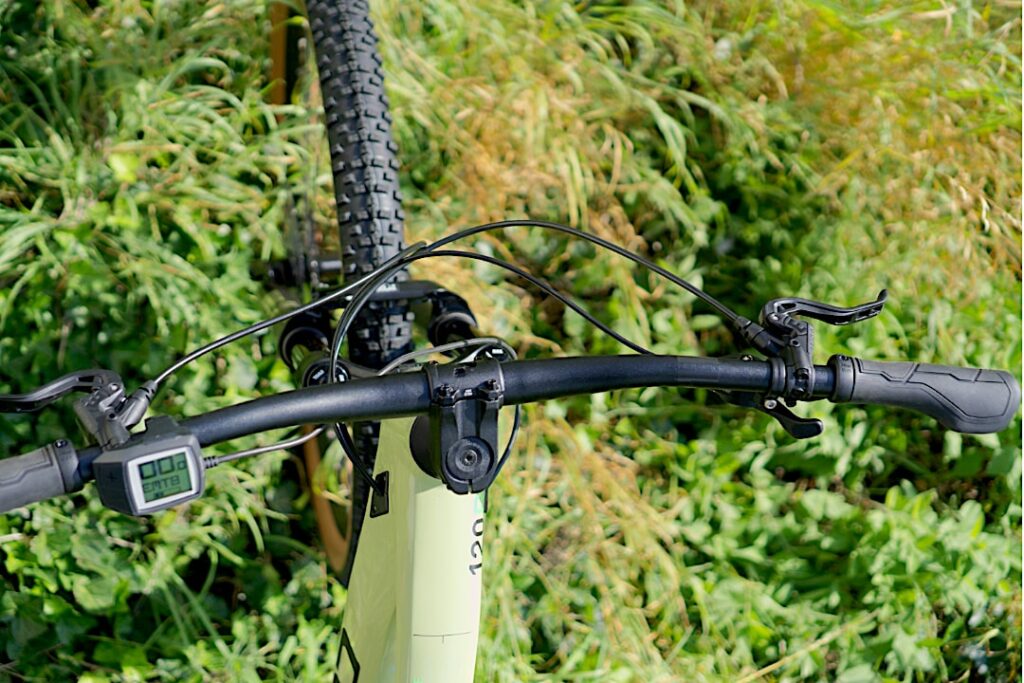 Cockpit des Cube Stereo Hybrid 120 Race 625 2022 mit Display und Lenker in grüner Umgebung.