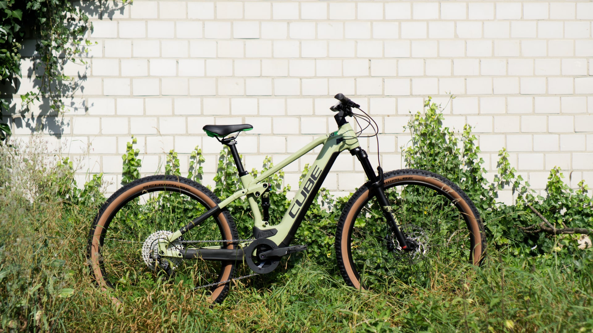 Cube Stereo Hybrid 120 Race 625 2022 E-Mountainbike vor weißer Ziegelwand, umgeben von grüner Vegetation.