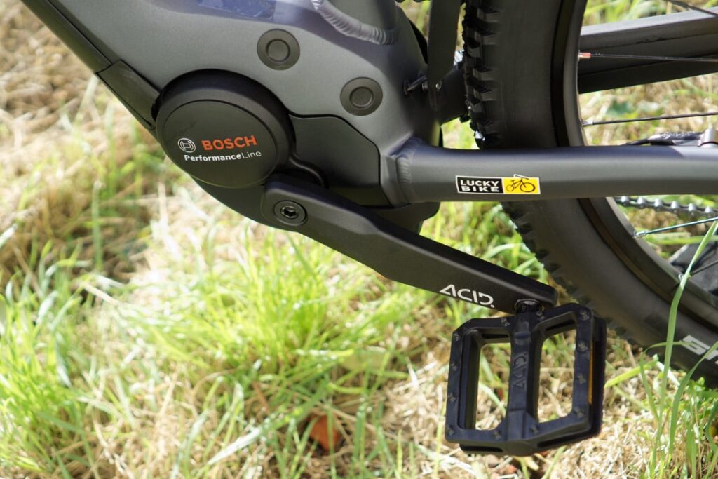 Bosch Performance Line Motor am Cube E-Bike mit Lucky Bike Logo, Detailansicht der Kurbel und Pedale auf Gras.