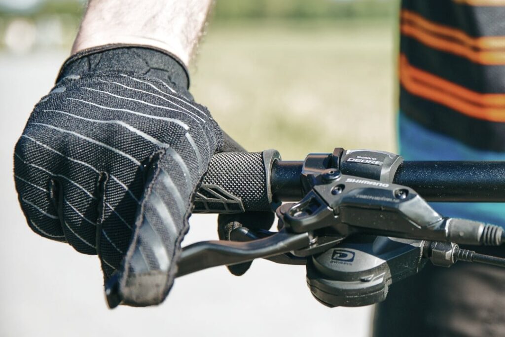 Nahaufnahme eines Fahrradbremshandgriffs mit Handschuh, Fokus auf Scheibenbremshebel und mögliche Wartungsprobleme.