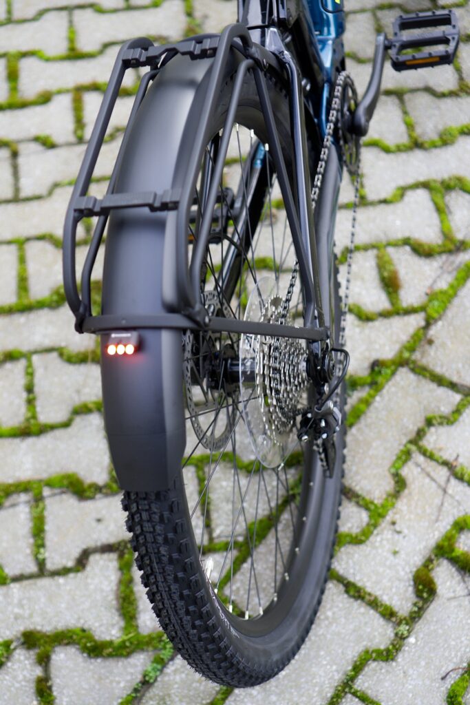 Hinterradansicht eines Trek Powerfly FS 4 Equipped 2022 mit Schutzblech und Rücklicht auf gepflastertem Weg.