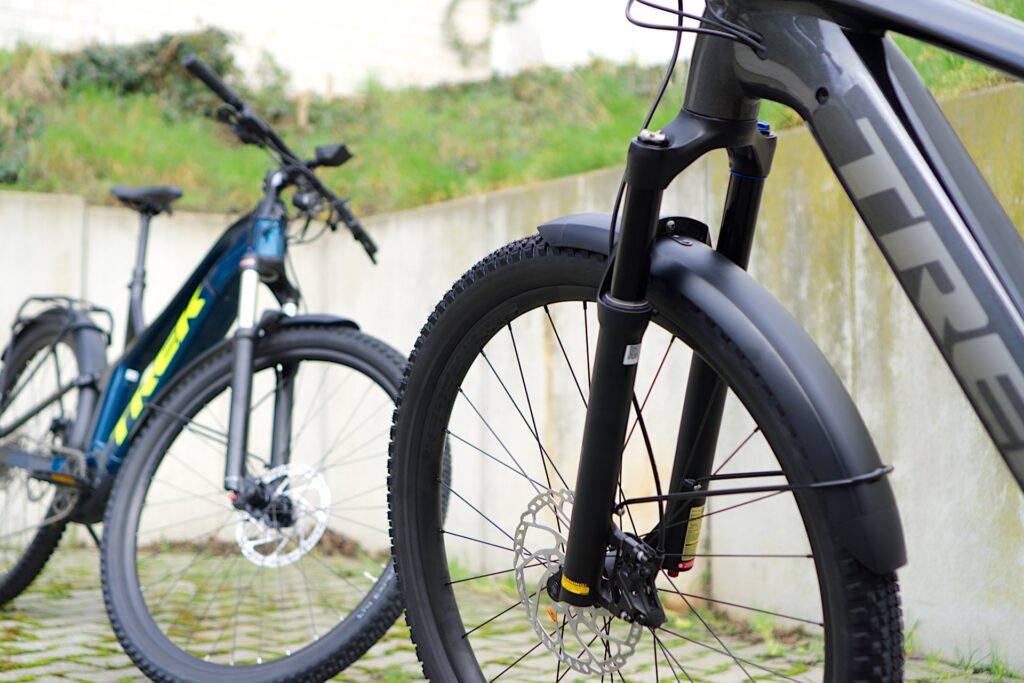 Trek Powerfly 7 und FS 4 E-Bikes im Vergleich, Nahaufnahme der Federgabeln auf gepflastertem Untergrund.