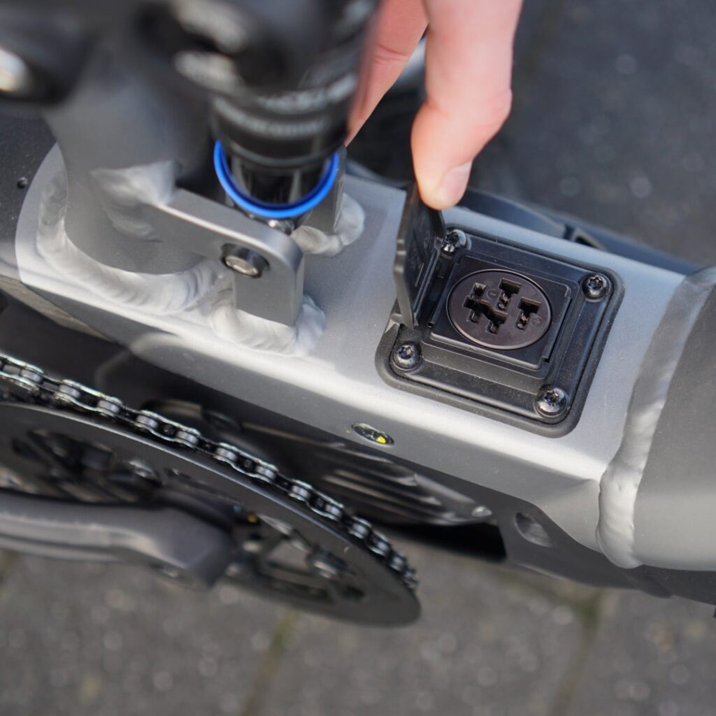 Ladeanschluss des Bergamont E-Horizon FS Expert 2022 wird geöffnet, Detailansicht am Fahrradrahmen.