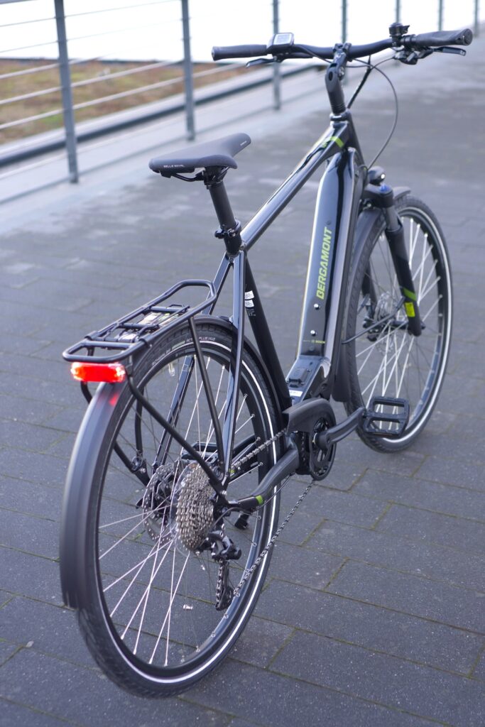 Bergamont E-Horizon Sport 2022 von hinten auf einem Gehweg, zeigt Gepäckträger und Hinterrad.