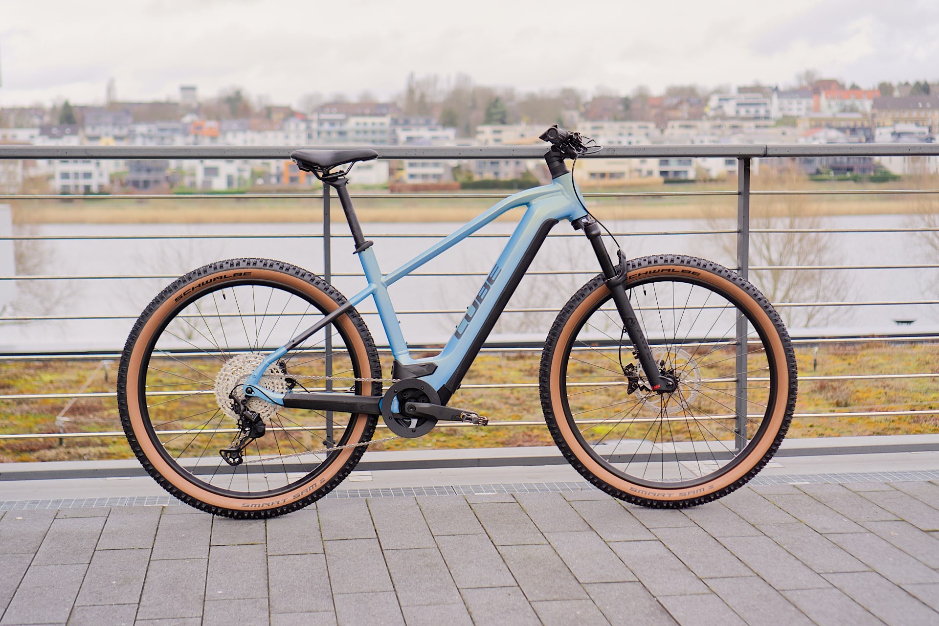 Cube Reaction Hybrid SL 750 2022 E-Bike, blau, auf Terrasse mit Stadtblick im Hintergrund.