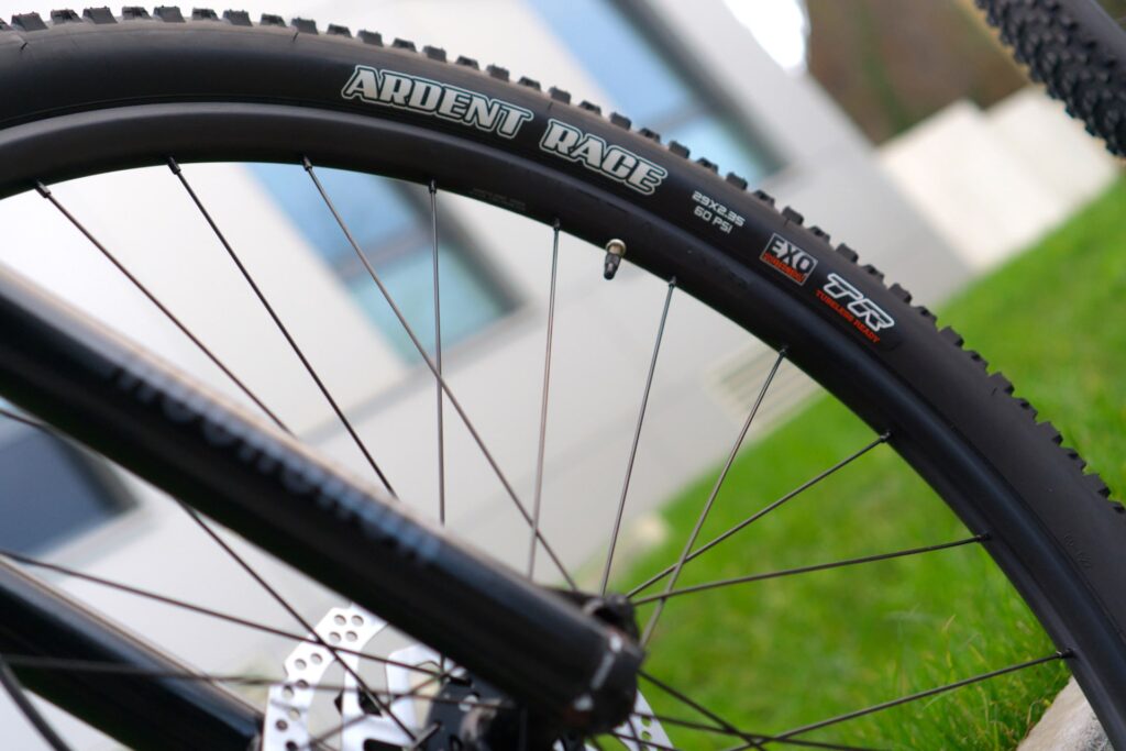 Maxxis Exo Reifen am Trek Marlin 8, Nahaufnahme des robusten Profils und der Speichen vor modernem Gebäude.