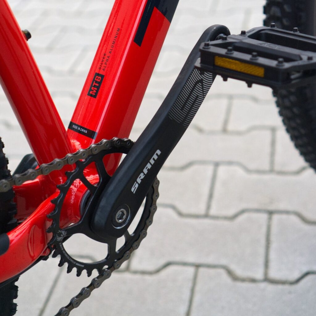 Trek Marlin 8 2022: Nahaufnahme des roten Aluminiumrahmens mit SRAM-Kurbel und Kette auf gepflastertem Boden.