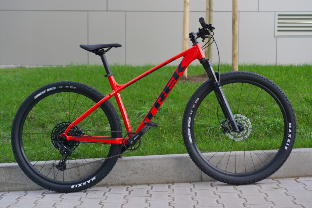 Rotes Trek Marlin 8 Mountainbike 2022 auf Gehweg vor grüner Wiese und grauer Wand.