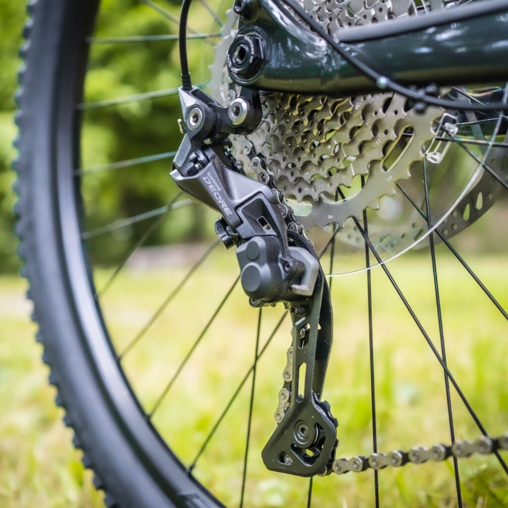 Shimano Deore Schaltwerk am Trek Powerfly 4 2022, Nahaufnahme des Hinterrads mit Kettenschaltung im Grünen.