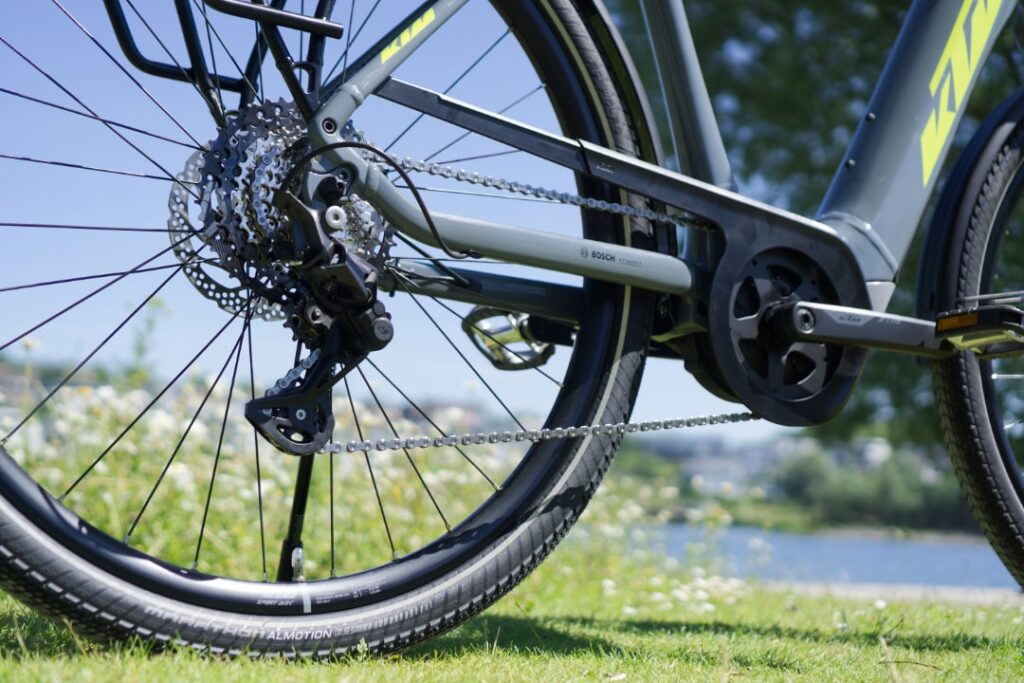 KTM Macina Sport Pro 2022 Antrieb mit Bosch-Motor, Nahaufnahme der Fahrradkette und Hinterrad auf grünem Rasen.