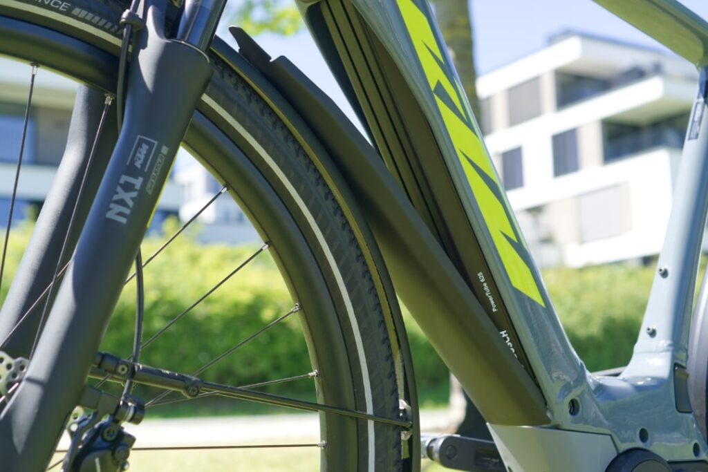 Detailaufnahme des KTM Macina Sport Pro 2022 mit Bosch Powertube 625 und NX1 Gabel im Hintergrund moderner Architektur.