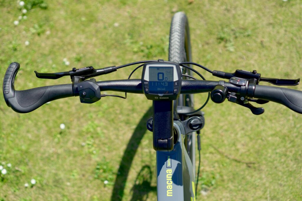 KTM Macina Sport Pro 2022 Cockpit mit Bosch-Display und ergonomischen Griffen auf grünem Hintergrund.