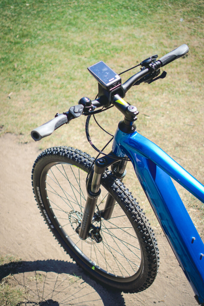 Blaues Axess Element 2022 Mountainbike auf einem Feldweg, Nahaufnahme des Lenkers mit montiertem Smartphone.