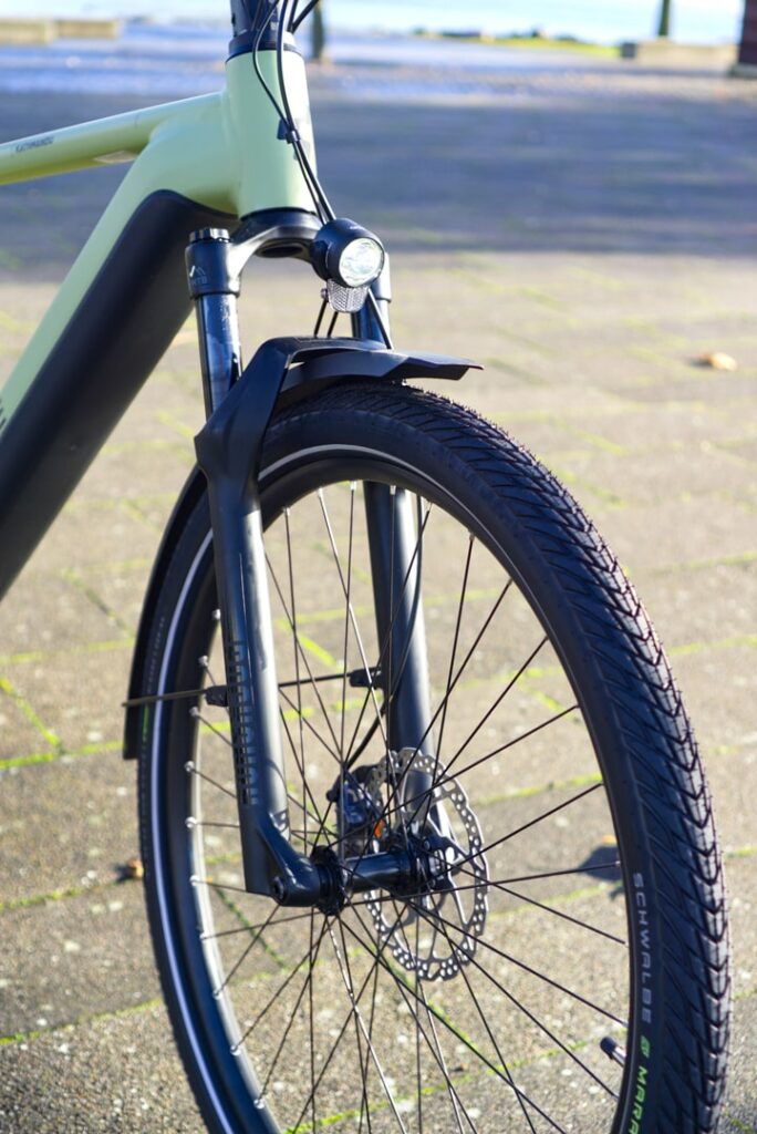 Federgabel des Cube Kathmandu Hybrid SLX 750 2023 mit Vorderlicht und Scheibenbremse auf Pflastersteinen.