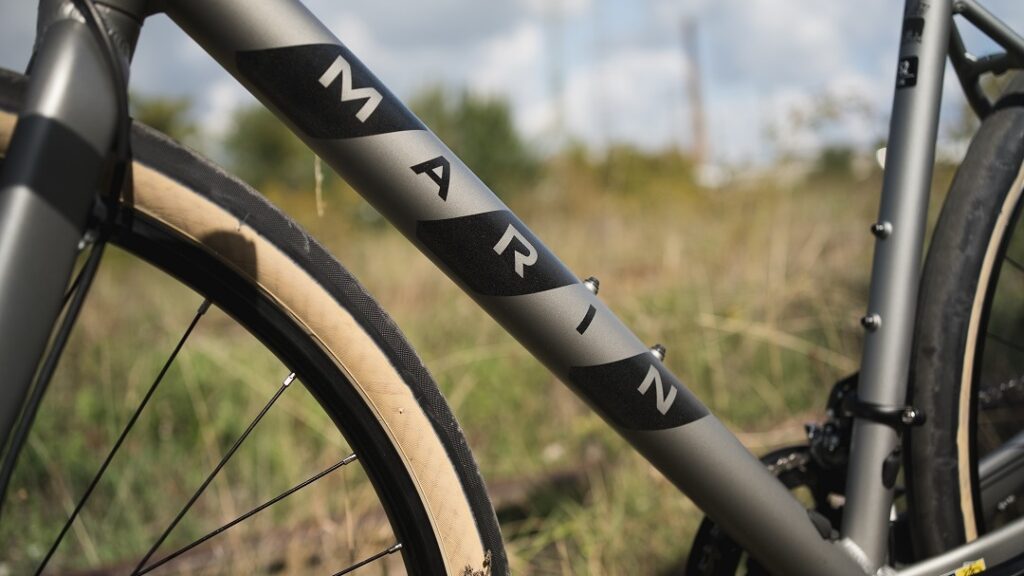 Graues Fahrrad mit "Marin"-Schriftzug am Rahmen, im Freien vor unscharfem Hintergrund.