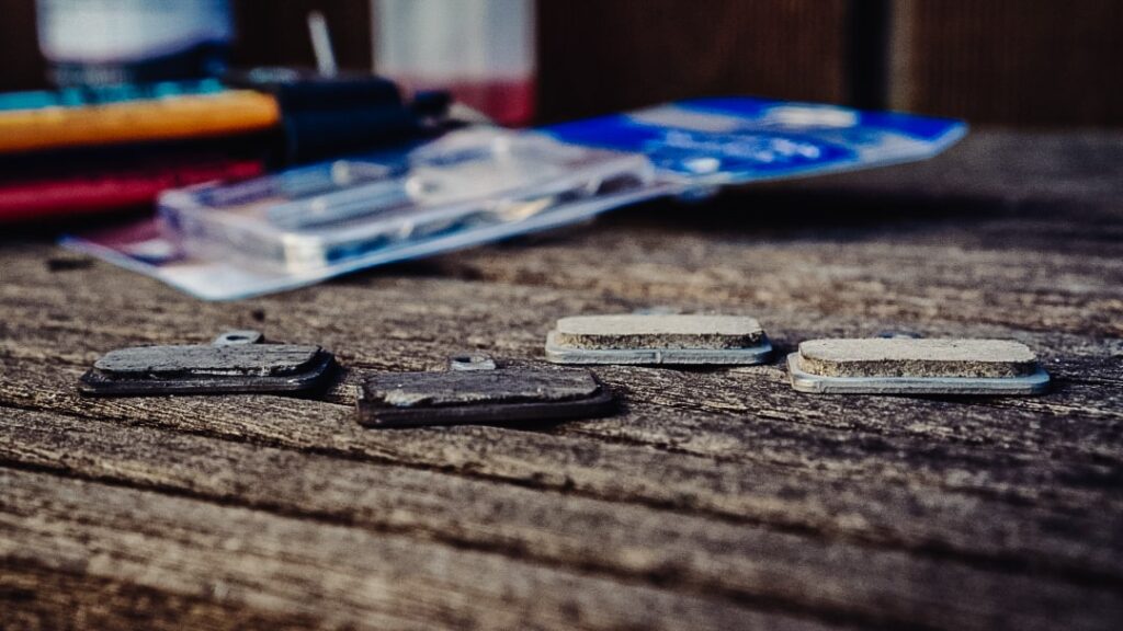 Vergleich von alten und neuen Scheibenbremsbelägen auf Holztisch, ideal für den Fahrrad-Frühjahrscheck.