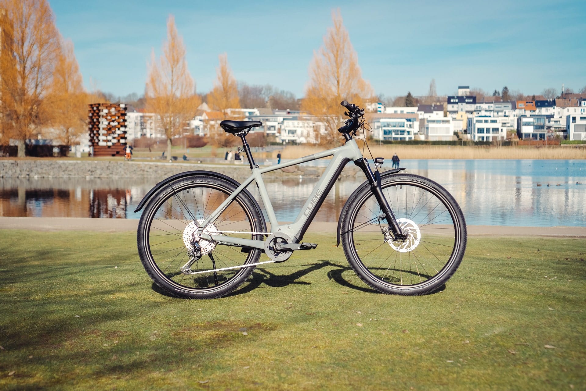 Cube Nuride Hybrid SLX 750 Allroad 2023 vor See und moderner Architektur im Hintergrund.