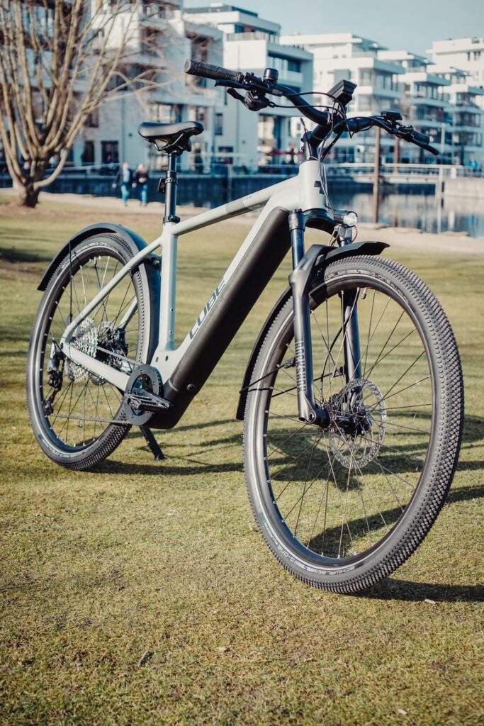 Cube Nuride Hybrid SLX 750 Allroad 2023 auf Rasen vor modernen Gebäuden, betont urbane Vielseitigkeit und Design.