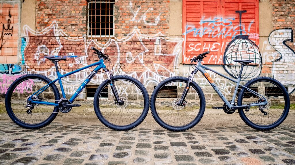 Zwei Marin Bolinas Ridge Mountainbikes vor bunter Graffiti-Wand auf Kopfsteinpflaster.