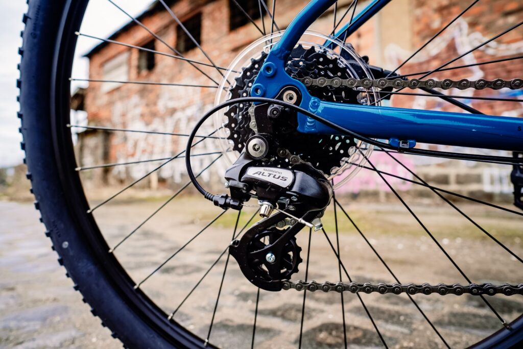 Shimano Altus Schaltwerk an einem blauen Fahrrad vor einer alten Backsteinmauer.