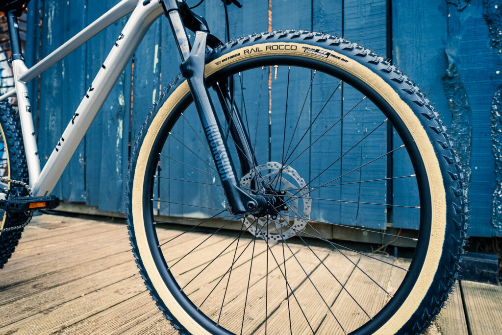 Vorderrad des Marin Team Marin 1 2023 mit RockShox-Gabel und Vee Tire Co. Reifen vor blauer Holzwand.