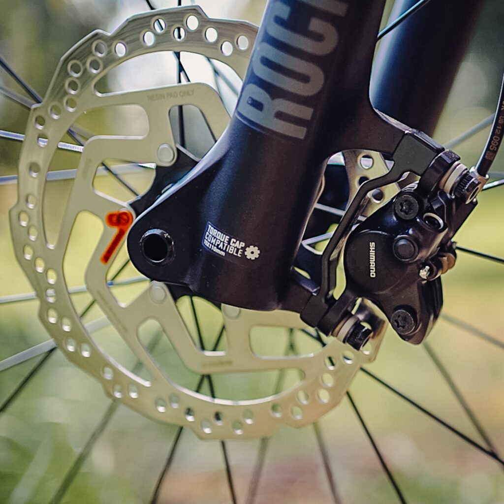 Shimano-Scheibenbremse am Trek Roscoe 7 2023, Nahaufnahme der Bremse und Gabel bei Tageslicht.