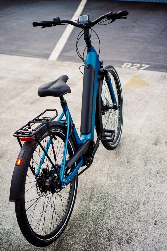 Cube Supreme RT Hybrid EXC 2023 in Blau, E-Bike mit Gepäckträger und integriertem Display, auf Asphalt geparkt.