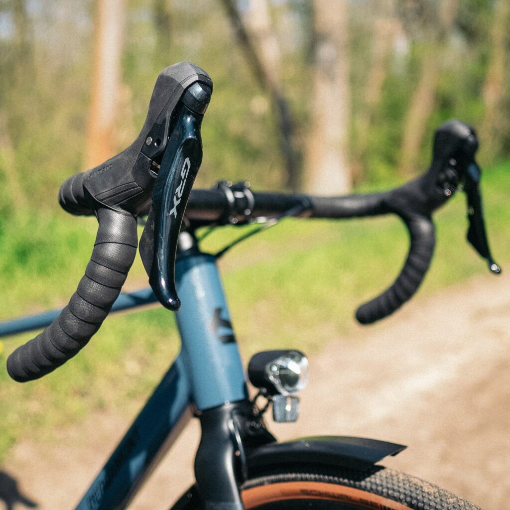 Bergamont Grandurance RD 5 2023 mit GRX-Schalthebel, Nahaufnahme des Lenkers auf einem sonnigen Waldweg.