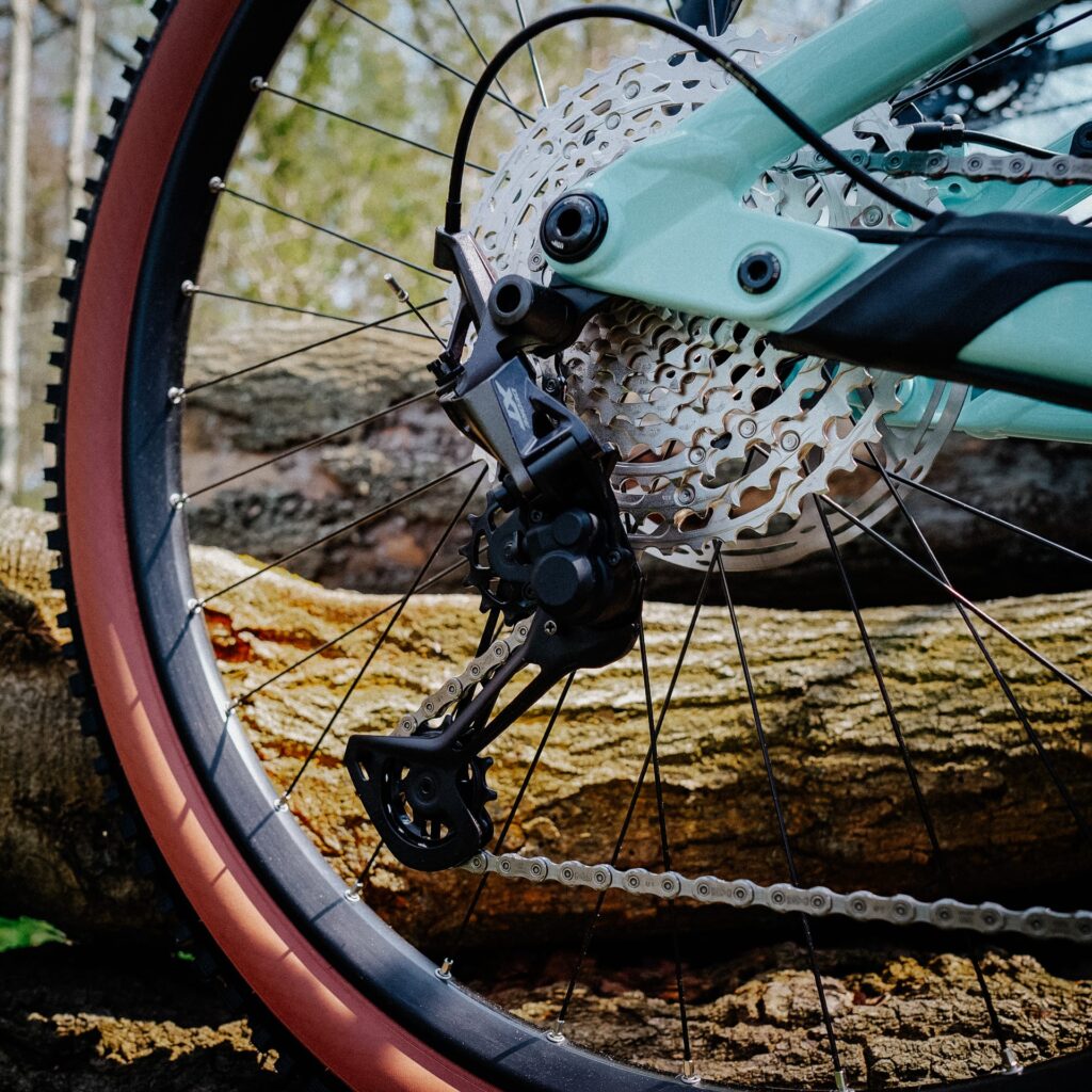 Shimano XT Schaltwerk an Cube Stereo Hybrid 140 HPC 2023, Detailansicht des Hinterrads vor einem Baumstamm.