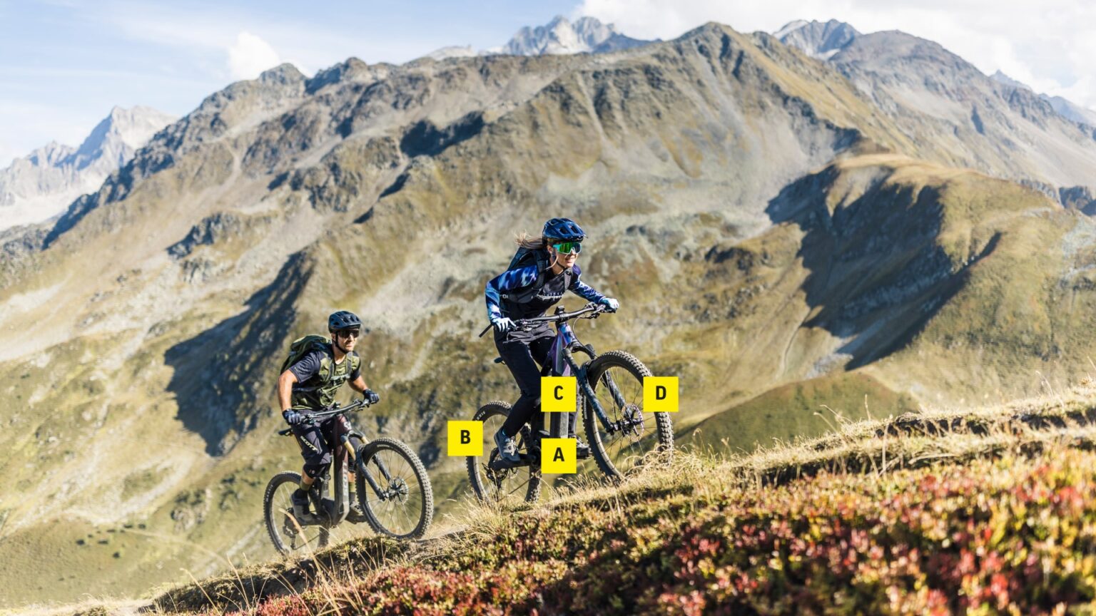 E-MTB-Fahrer erklimmen steilen Bergpfad mit Fully-Bikes, umgeben von majestätischer Bergkulisse.