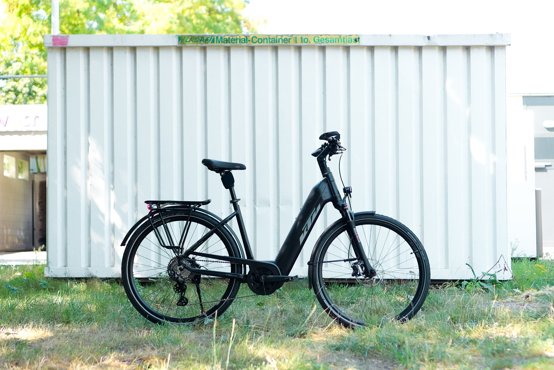 KTM Macina Style Pro 2024 E-Bike vor weißem Container, seitliche Ansicht, auf Gras stehend.