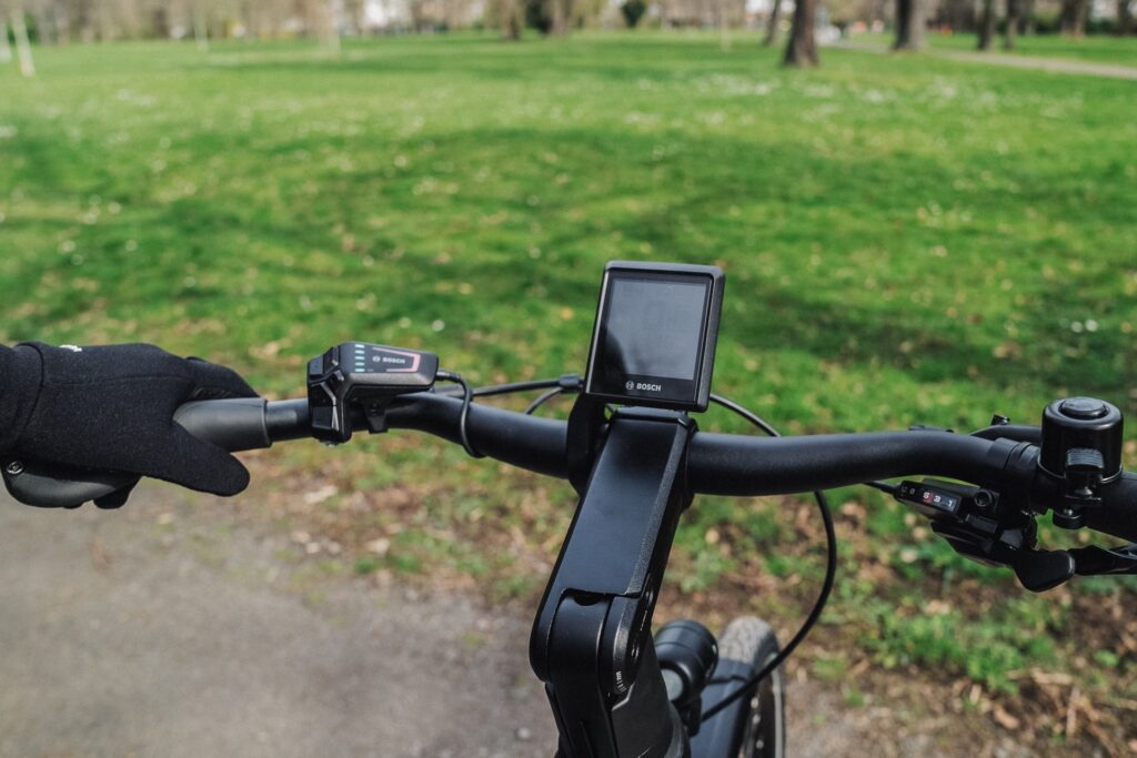 KTM Macina Style Pro 2024 Cockpit mit Bosch Intuvia 100 Display in grüner Parkumgebung.