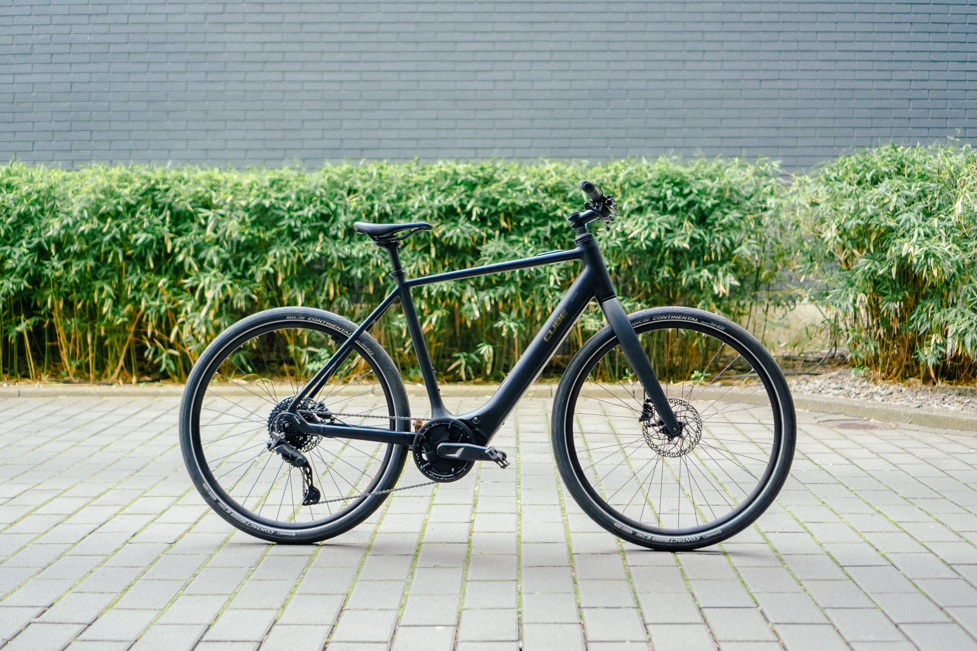 Cube Editor Hybrid Pro 400X E-Bike auf gepflastertem Weg vor grüner Hecke, modernes Design, seitliche Ansicht.