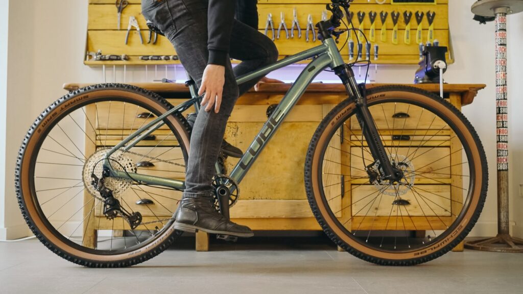 Person auf Fahrrad demonstriert richtige Sattel- und Lenkerhöhe für komfortable Sitzposition, Werkzeuge im Hintergrund.