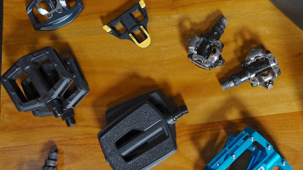 Verschiedene Fahrradpedale auf Holztisch zur optimalen Einstellung für Komfort und schmerzfreies Fahren.