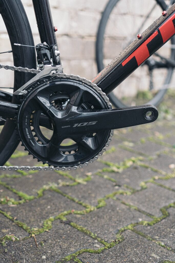 Shimano 105 Kurbelgarnitur an einem Trek-Rennrad auf nassem Pflaster, Detailansicht der Antriebskomponenten.