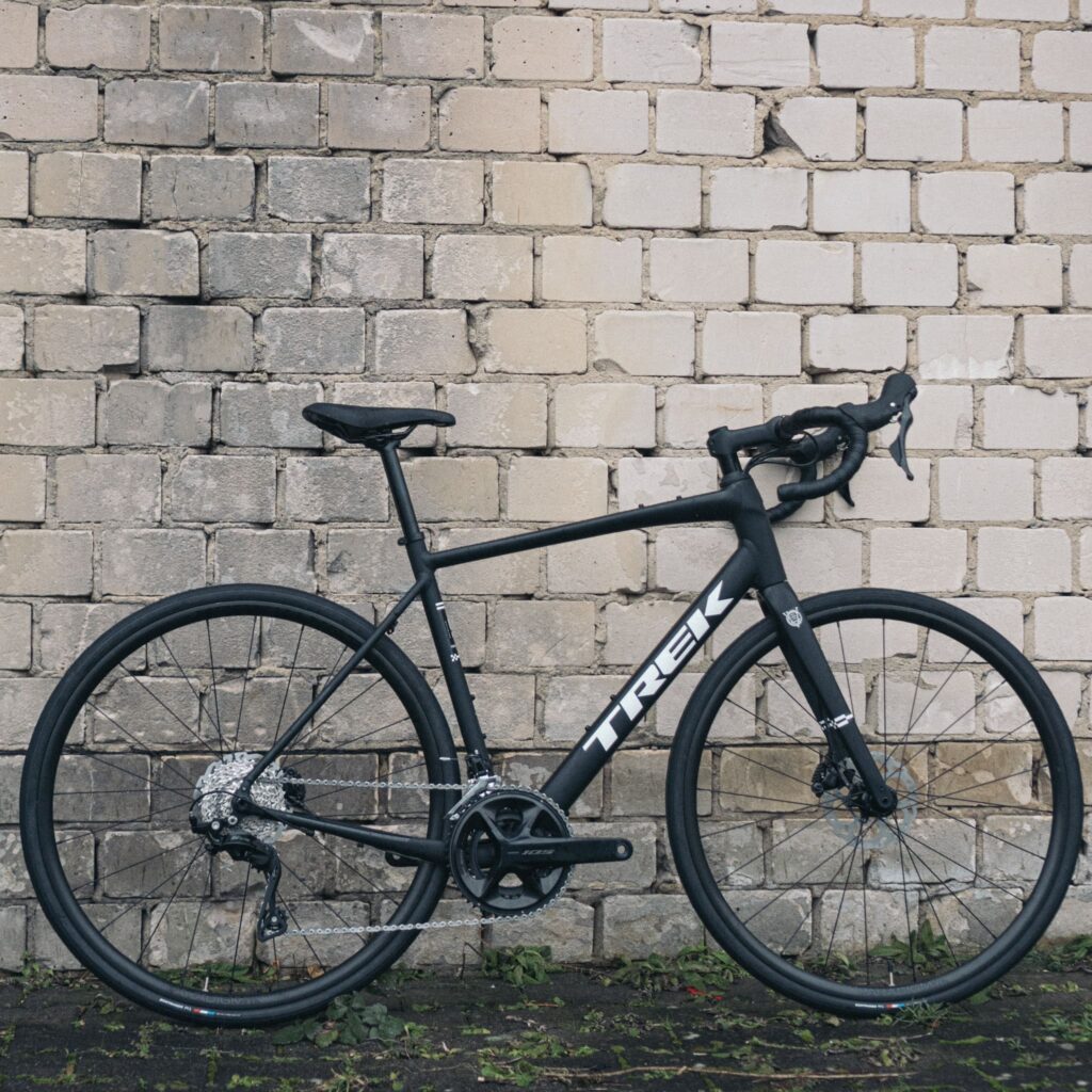 Schwarzes Trek-Rennrad lehnt an einer Ziegelwand, seitliche Ansicht, Fokus auf Rahmen und Komponenten.