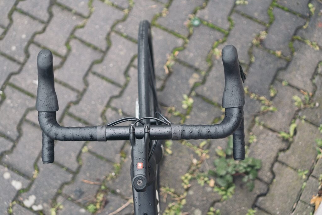Trek Domane AL 5 Cockpit bei Regen auf Kopfsteinpflaster, Fokus auf Lenker und Bremshebel, Detailansicht.