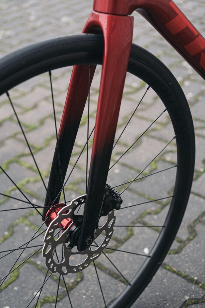 Rote Gabel eines Rennrads mit Scheibenbremse auf Kopfsteinpflaster.