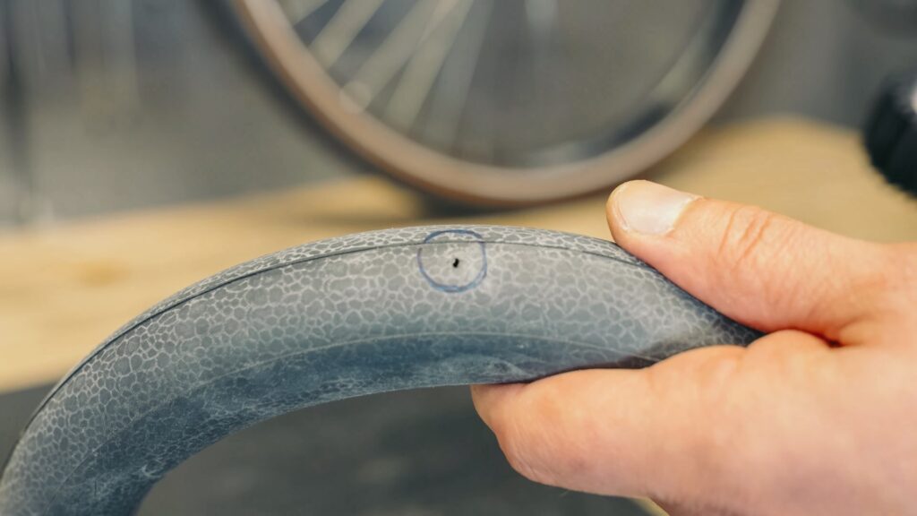 Fahrradschlauch mit markiertem Loch zur Reparatur in Nahaufnahme, Hand hält den Schlauch.