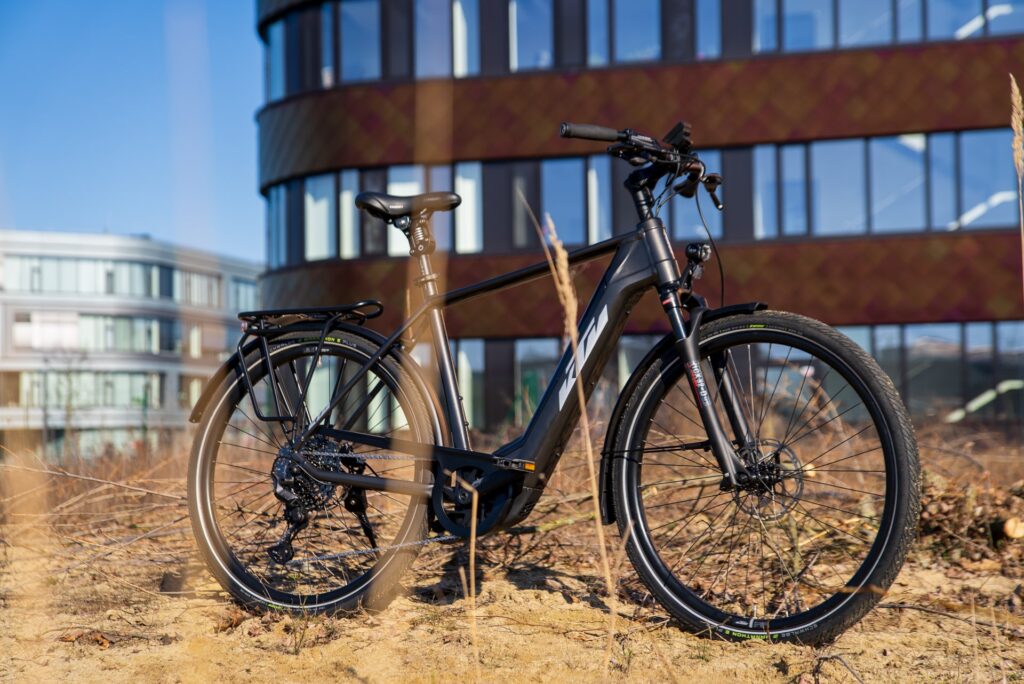 KTM MACINA Style E-Bike vor modernem Bürogebäude, seitliche Ansicht, Fokus auf Rahmen und Räder.