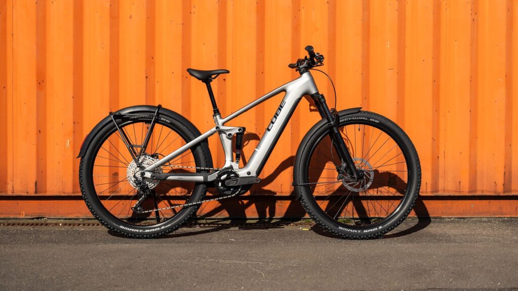 Cube Stereo Hybrid 2025 Modell vor orangefarbener Wand, seitliche Ansicht, zeigt modernes Design und Ausstattung.