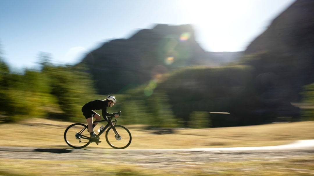 Rennradfahrer in Bewegung vor Berglandschaft, Symbol für Geschwindigkeit und Outdoor-Freude.