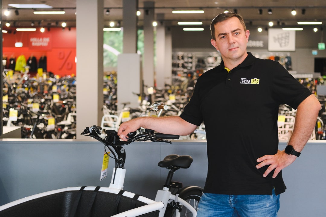 E-Lastenrad-Berater in Fahrradladen, umgeben von Fahrrädern; Tipps und Kaufberatung zu E-Lastenrädern.