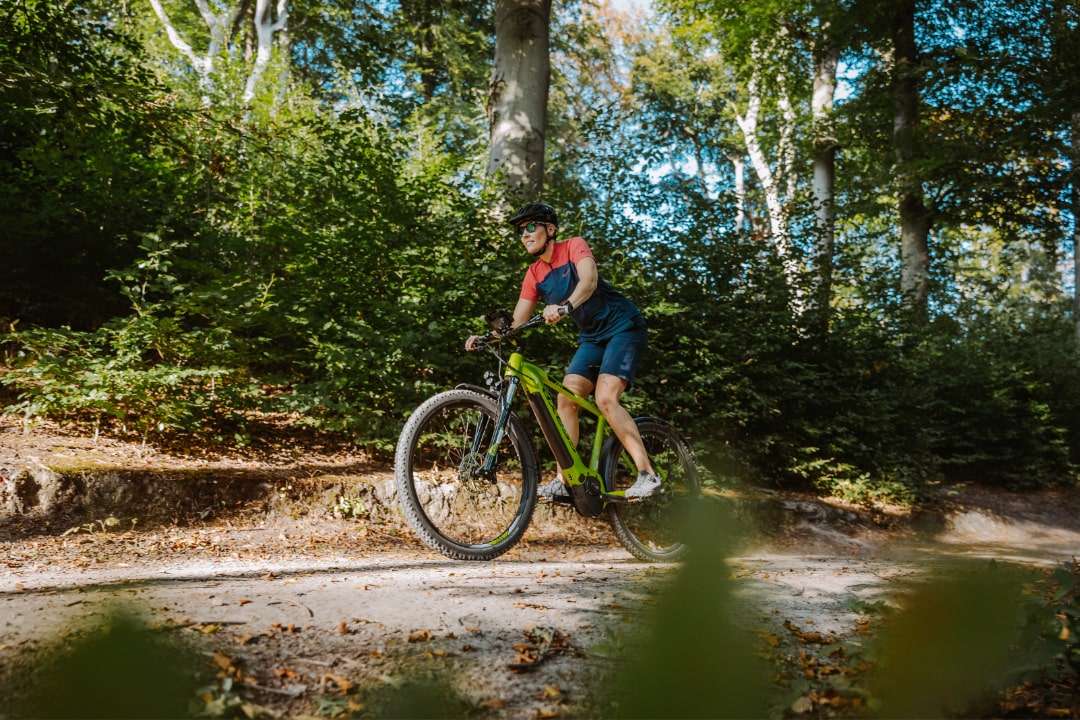 Radfahrer im Wald auf grünem E-MTB-Hardtail bei sonnigem Wetter, symbolisiert Fahrspaß und Naturerlebnis.