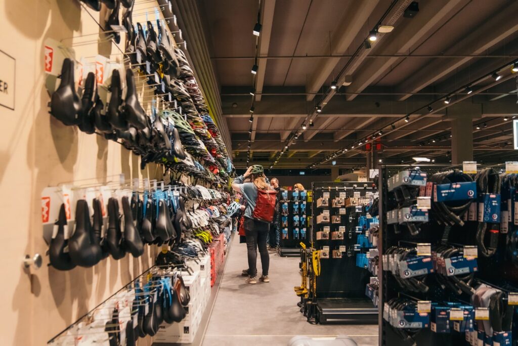 Auswahl an Fahrradzubehör in einem Fahrradgeschäft. Eine Frau probiert einen Helm an.