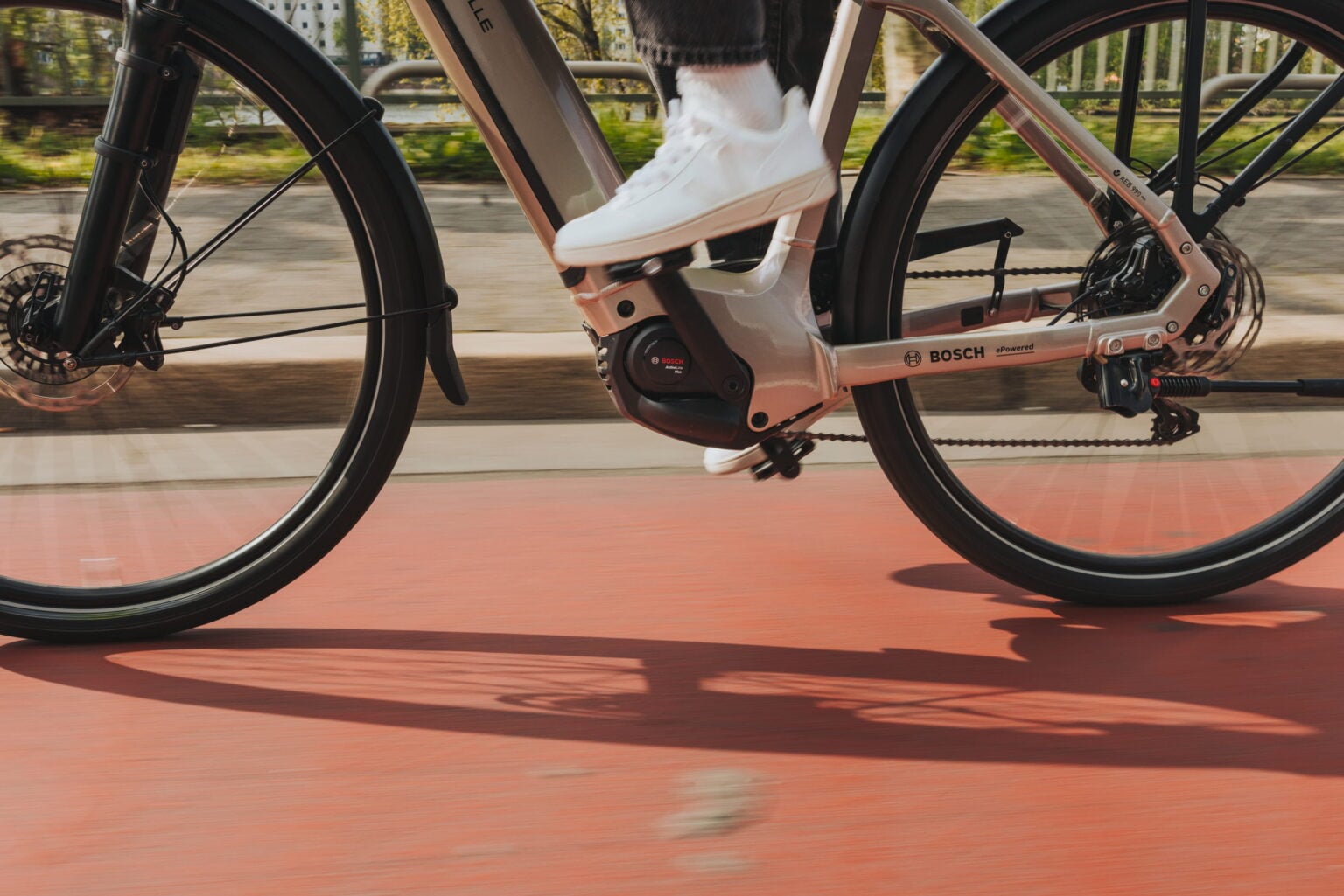 Nahaufnahme eines fahrenden E-Bikes auf einem Radweg, zu sehen sind Rahmen, Laufräder und der Bosch-Antrieb im Bereich der Hinterradnabe.